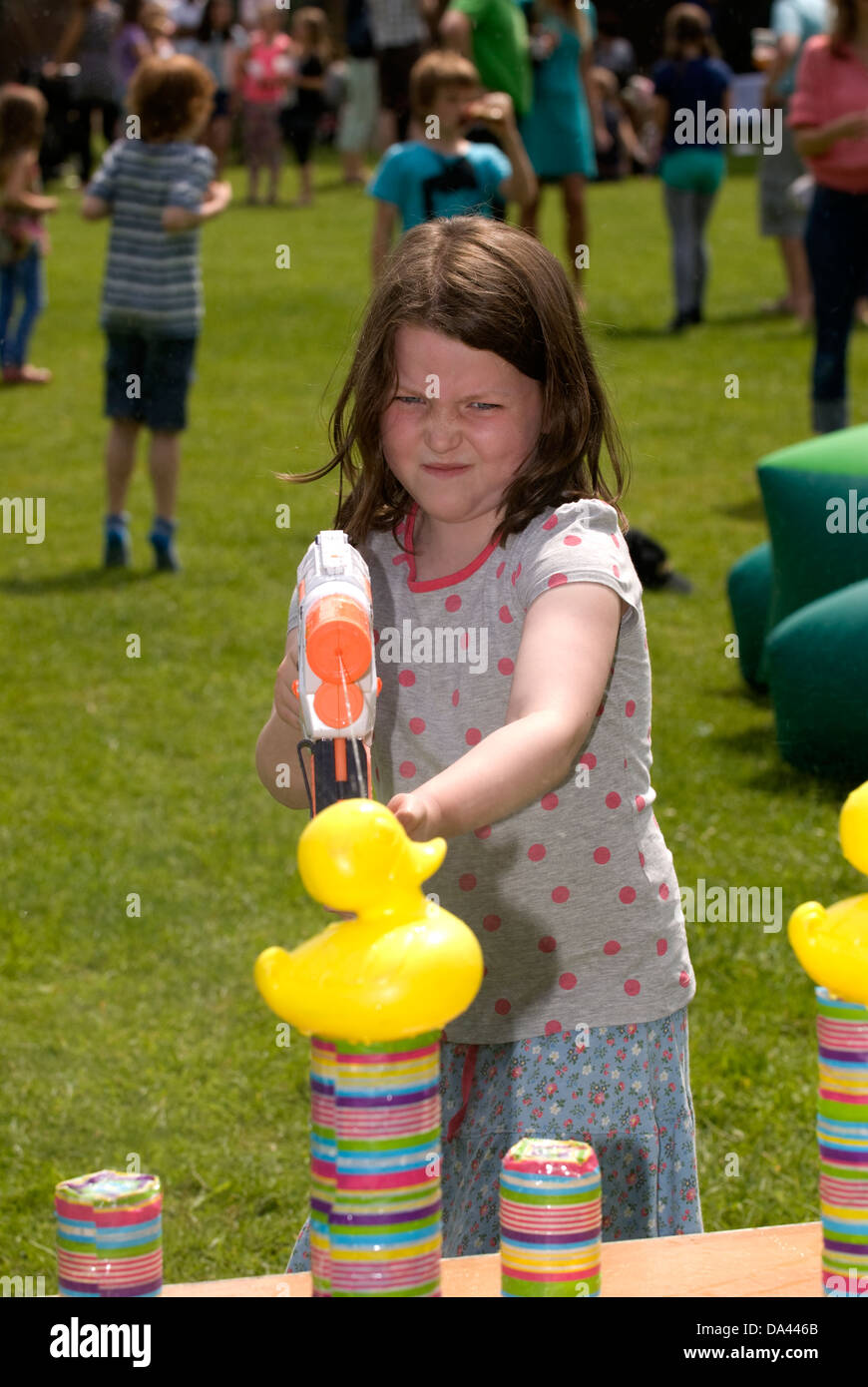 7 year old girl at summer fete using water pistol to squirt plastic ducks, Sheet, Hampshire, UK. Stock Photo