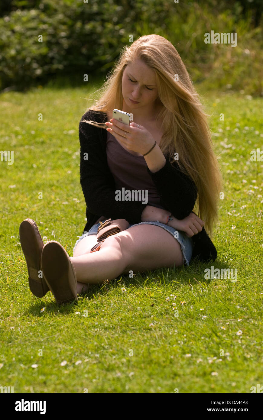 17 year old girl sitting on grass perusing mobile phone, Sheet, Hampshire, UK. Stock Photo