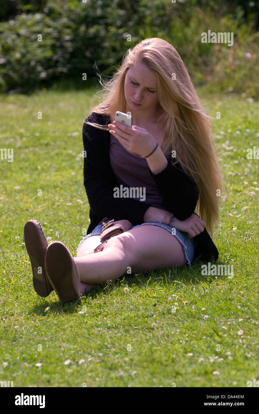 17 year old girl sitting on grass perusing mobile phone, Sheet, Hampshire, UK. Stock Photo