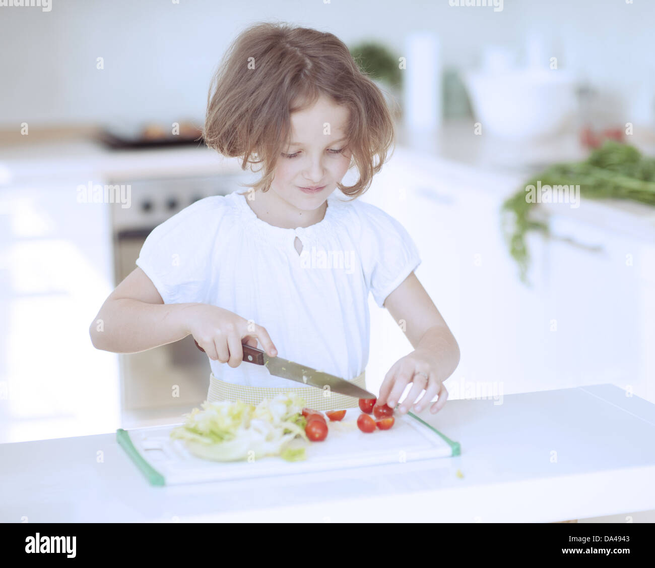 Young girl chopping tomatoes and making a salad in the kitchen Stock Photo