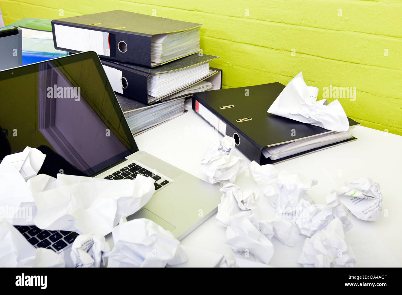 Close-up view of crumpled paper over laptop on desk with empty chair and folders Stock Photo