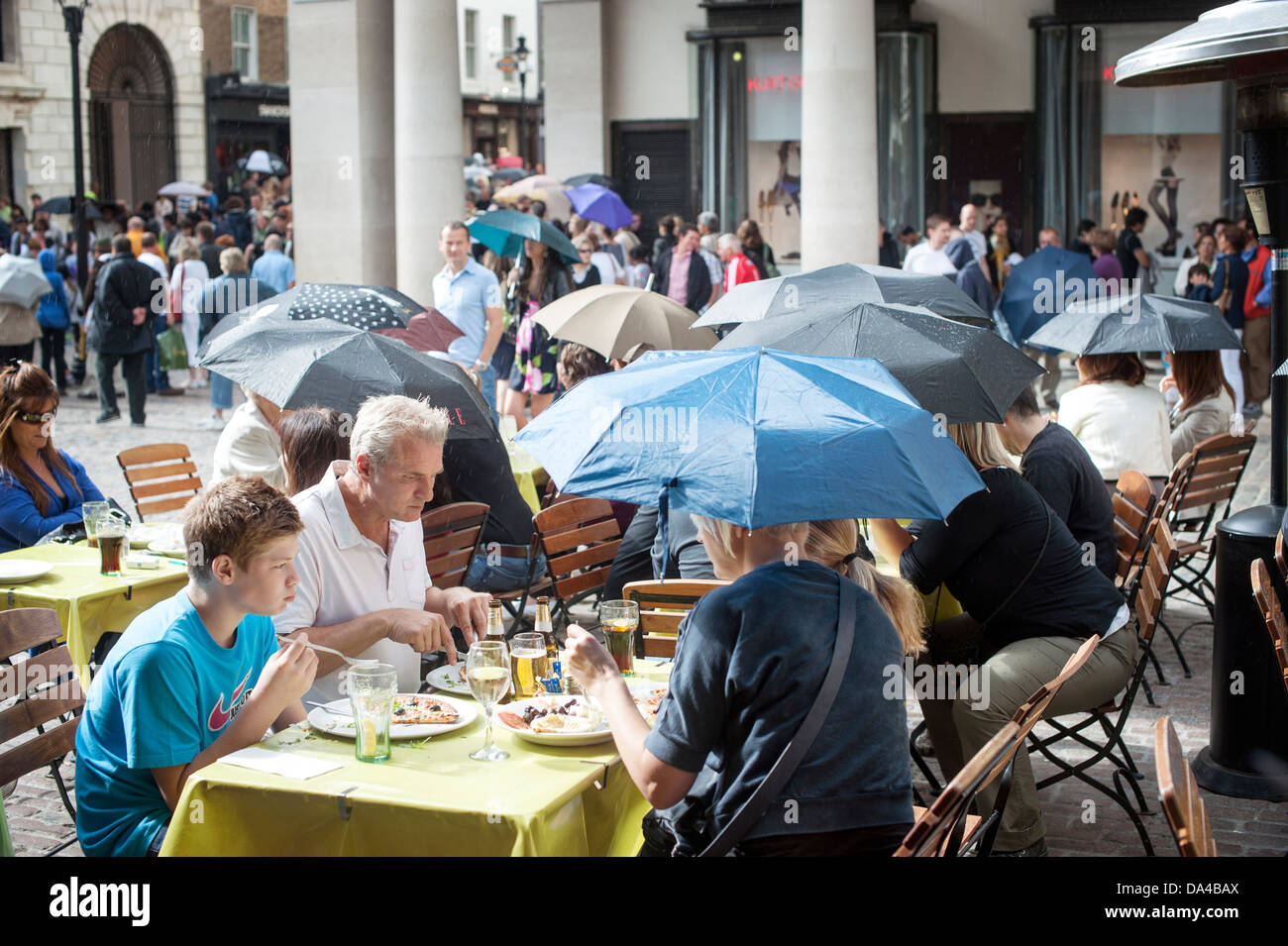 People eating al fresco in Covent garden under umbrellas  during rain shower Stock Photo