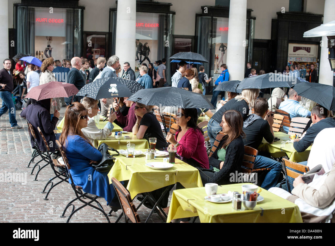 People eating al fresco in Covent garden under umbrellas  during rain shower Stock Photo