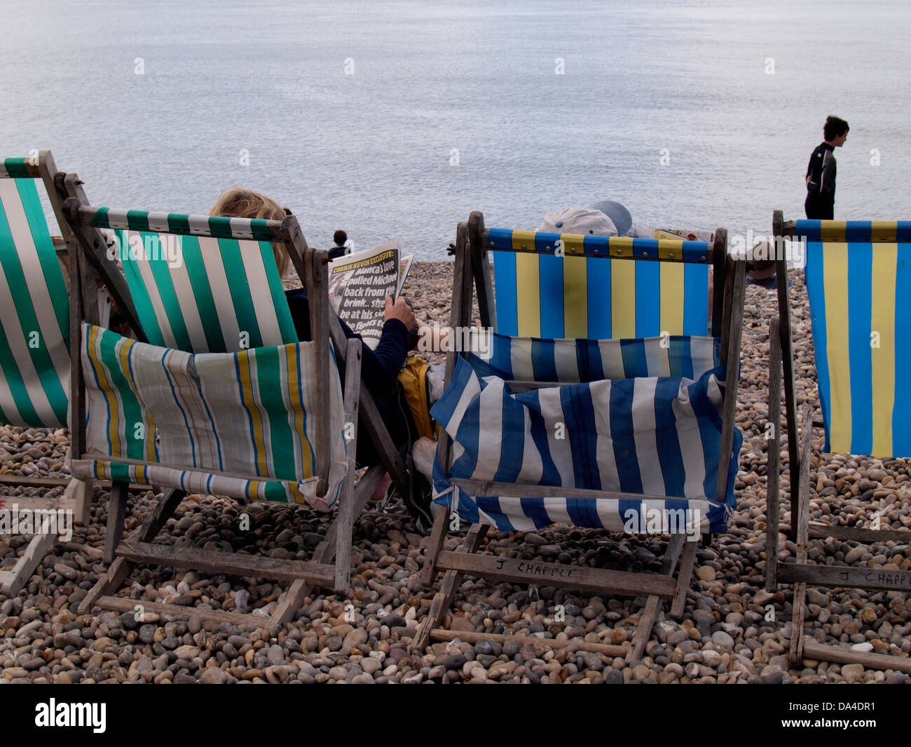 Couple sat in deckchairs at the beach reading newspapers, Beer, Seaton, UK 2013 Stock Photo