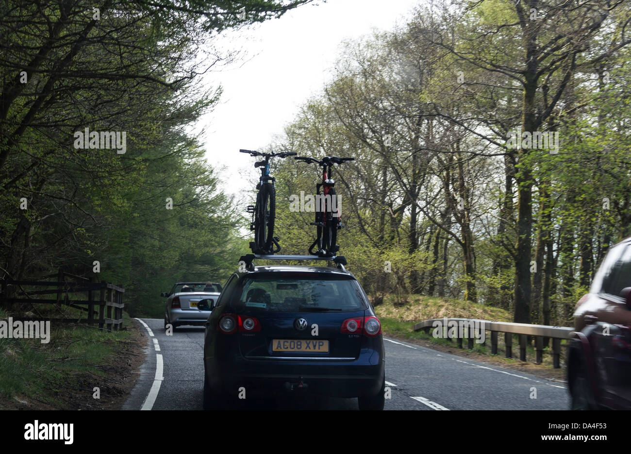 Car on a road in Scotland, with cycles mounted on the top. People go to a beautiful place and then do cycling over there. Stock Photo