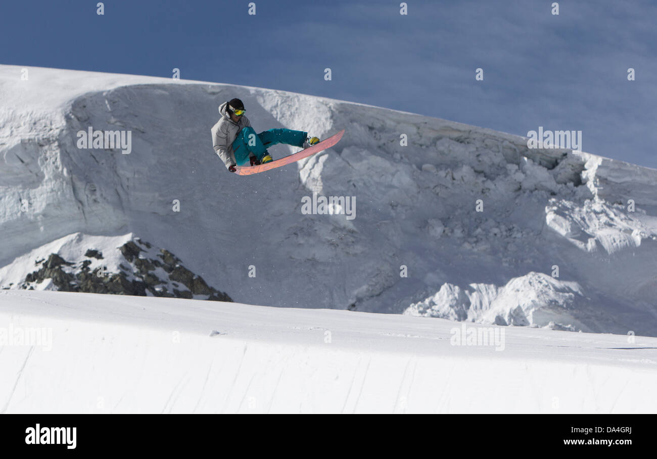 Professional snowboarder Reto Kestenholz executing a trick whilst jumping in the halfpipe in the summer snowpark on the Theodul glacier in Zermatt. Stock Photo