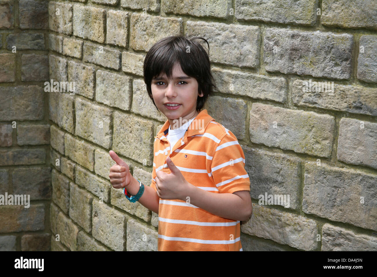Portrait of confident brunette boy giving thumbs up against stone wall Stock Photo