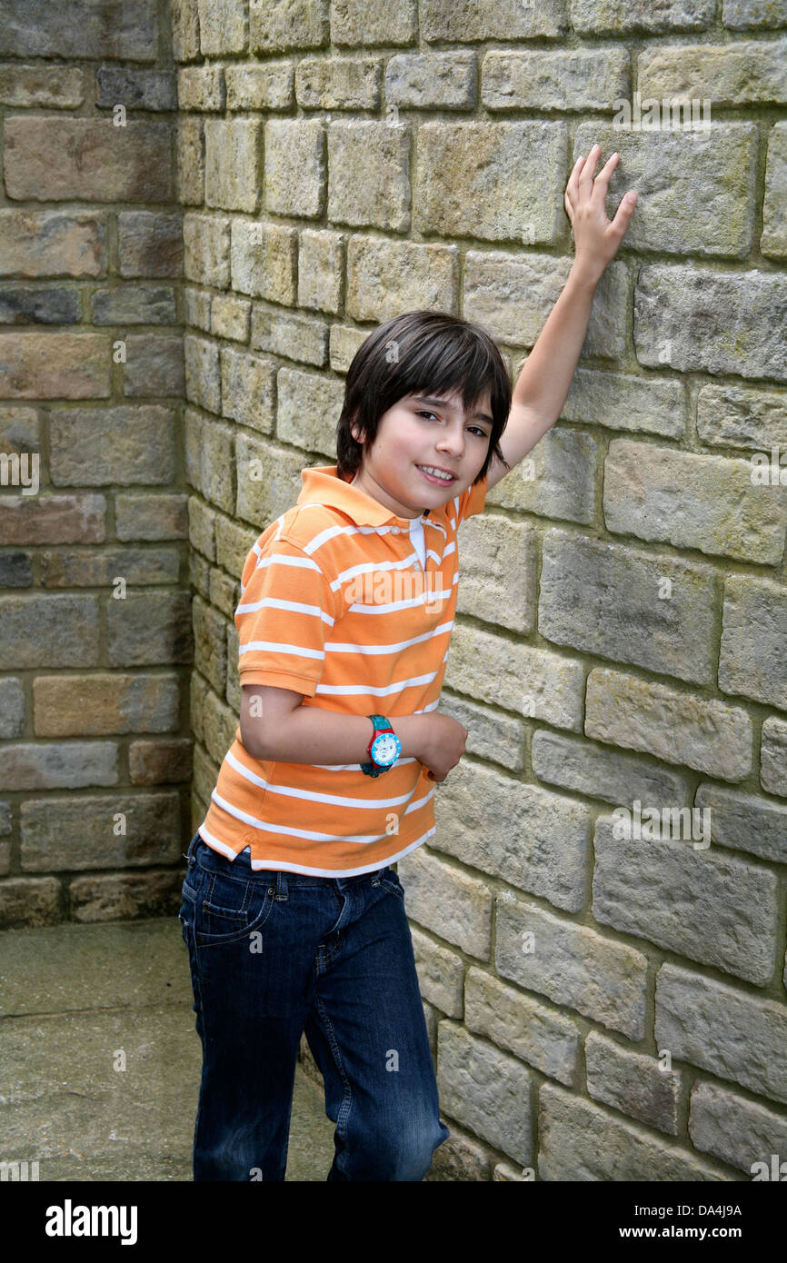 Portrait of smiling brunette boy leaning on stone wall with arms raised Stock Photo