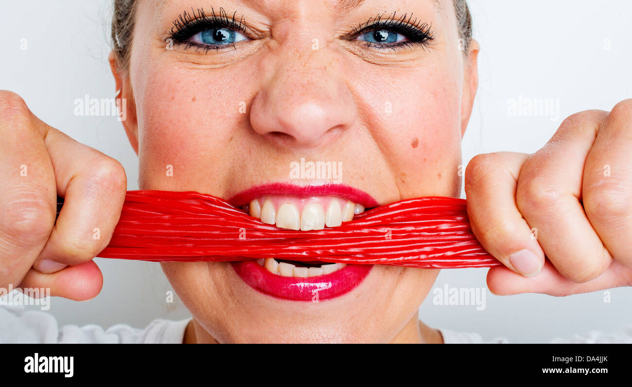A young woman eating lots of red liquorice lace sweets Stock Photo