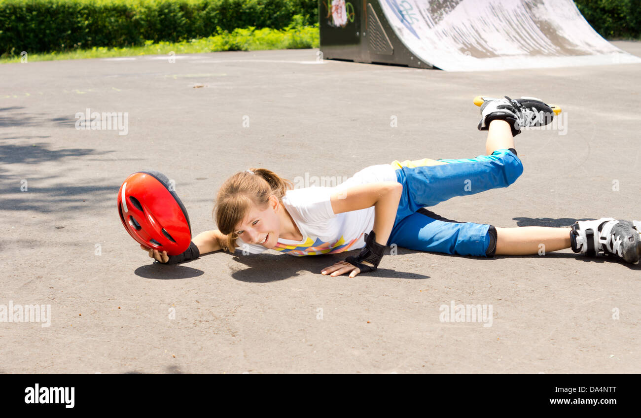 Young girl falling while roller skating lying sprawled on the tarmac with  her helmet in her hand and leg in the air Stock Photo - Alamy