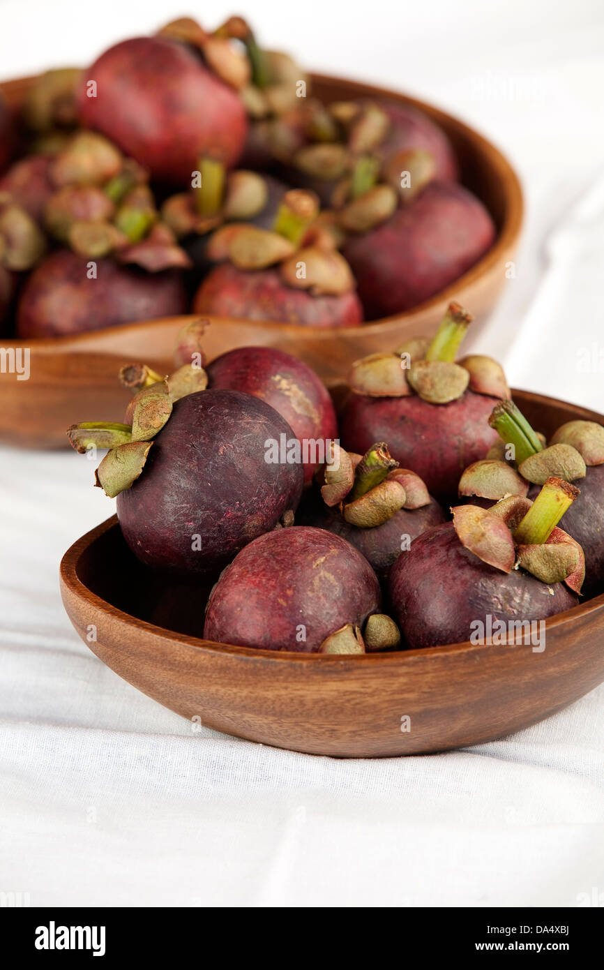 Bowls of fresh dark maroon/purple mangosteen fruits on a white surface