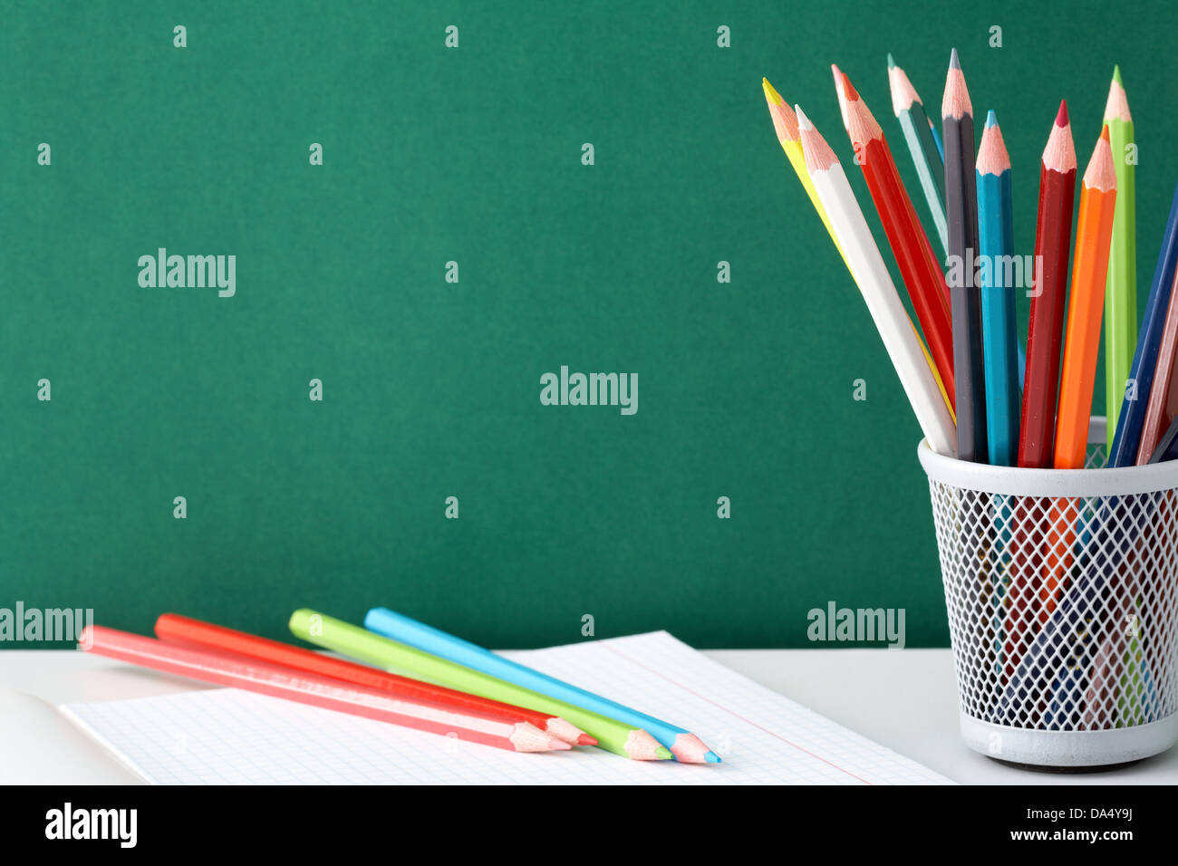 Stack of colorful pencils and open copybook near by on background of ...