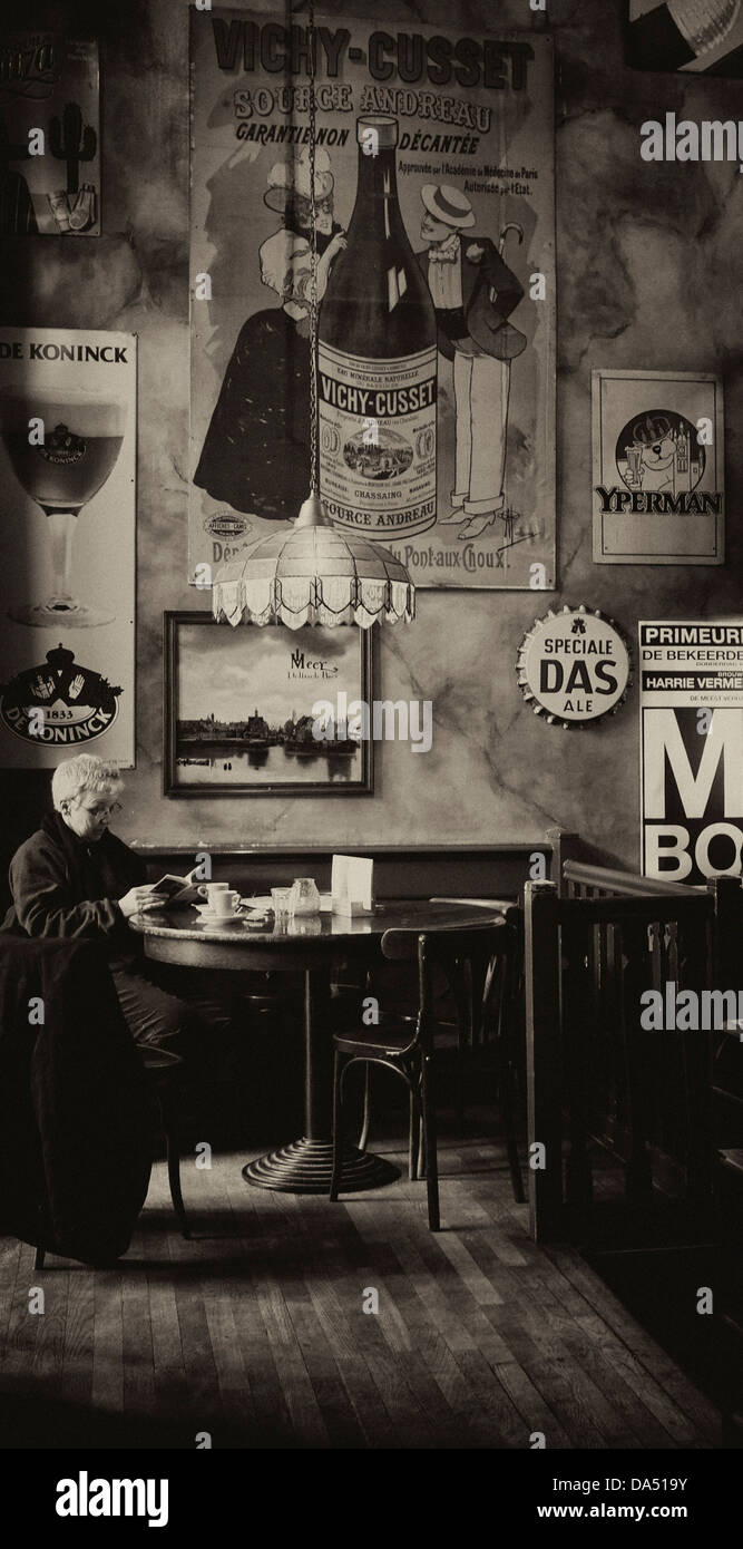 Black and white image of woman reading in an Amsterdam bar with retro signs on the walls Stock Photo