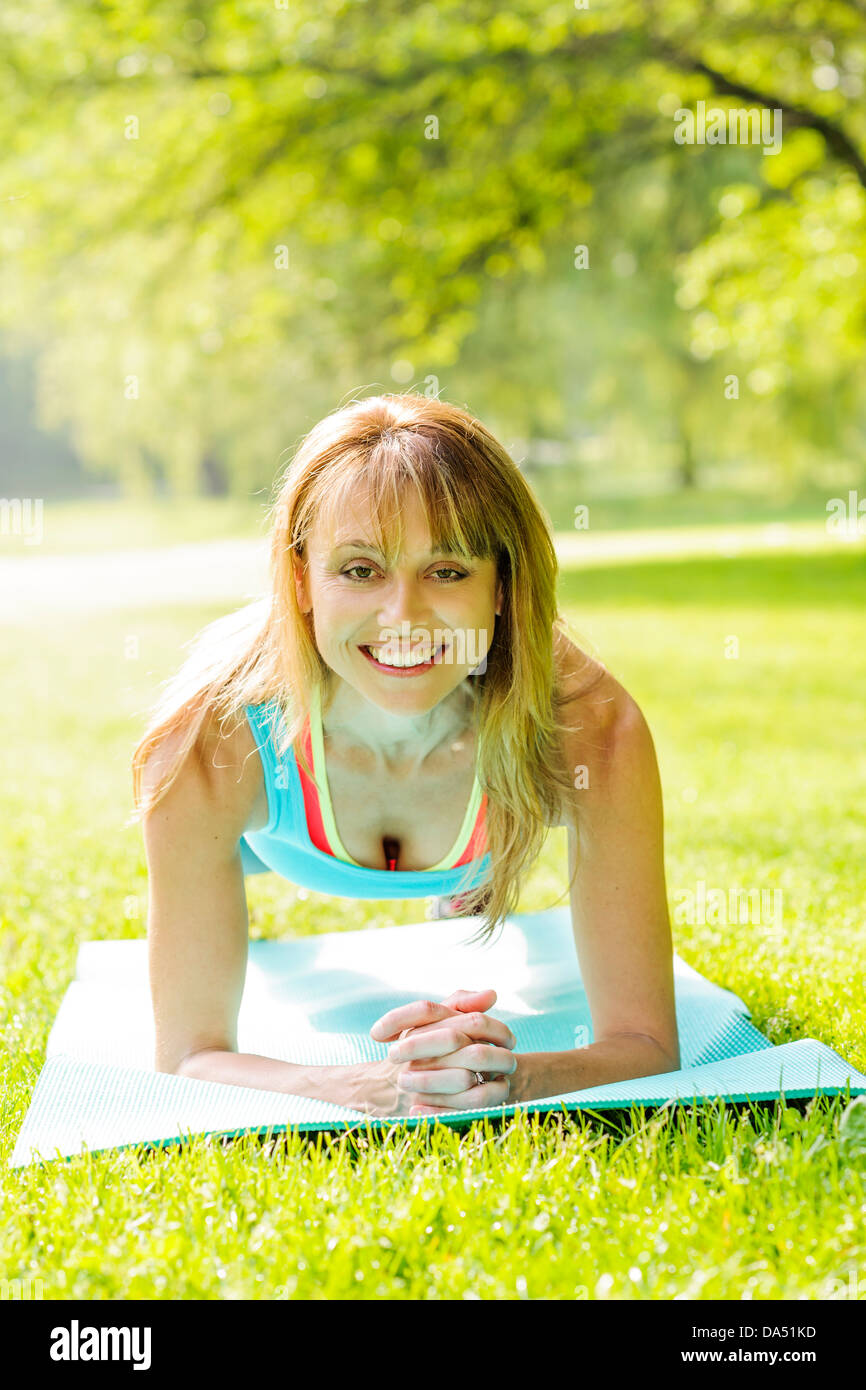Female fitness instructor holding plank pose exercising outside in green summer park Stock Photo