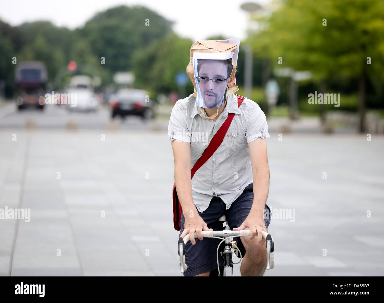 Berlin, Germany. 04th July, 2013. A democracy activist with a mask of the portrait of Edward Snowden cycles past the German Chancellery in Berlin, Germany, 04 July 2013. Snowden made the supposed data espionage of the USA and Great Britain public. Photo: KAY NIETFELD/dpa/Alamy Live News Stock Photo