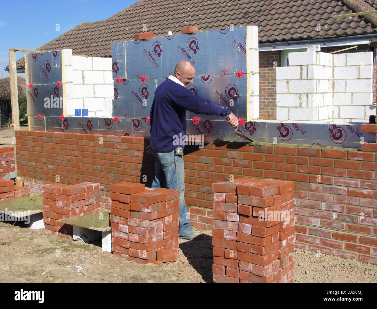 Builder cementing & building a brick wall with celotex thermal insulation board & cavity walls in an extension or new property Stock Photo