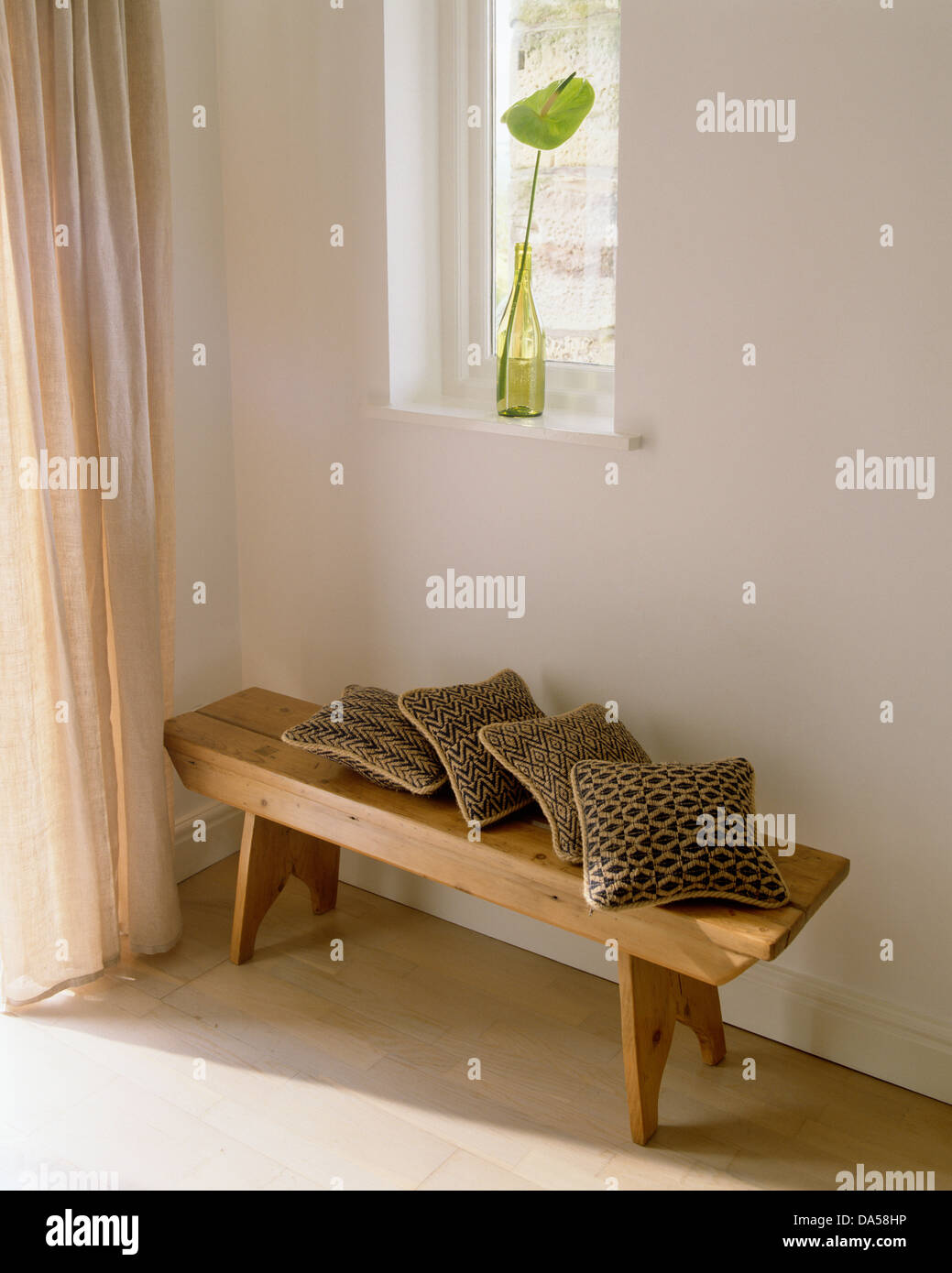 Brown cushions on rustic wooden bench below window in simple white hall  with beige drapes on the door Stock Photo - Alamy