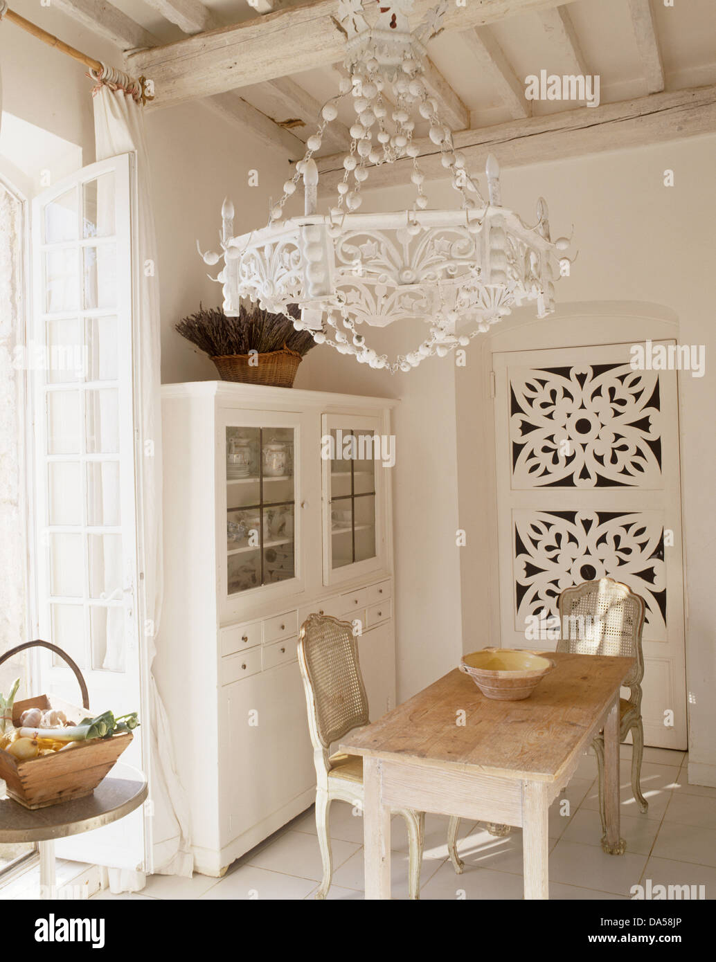 Ornate white light on white beamed ceiling above scrubbed wood table in