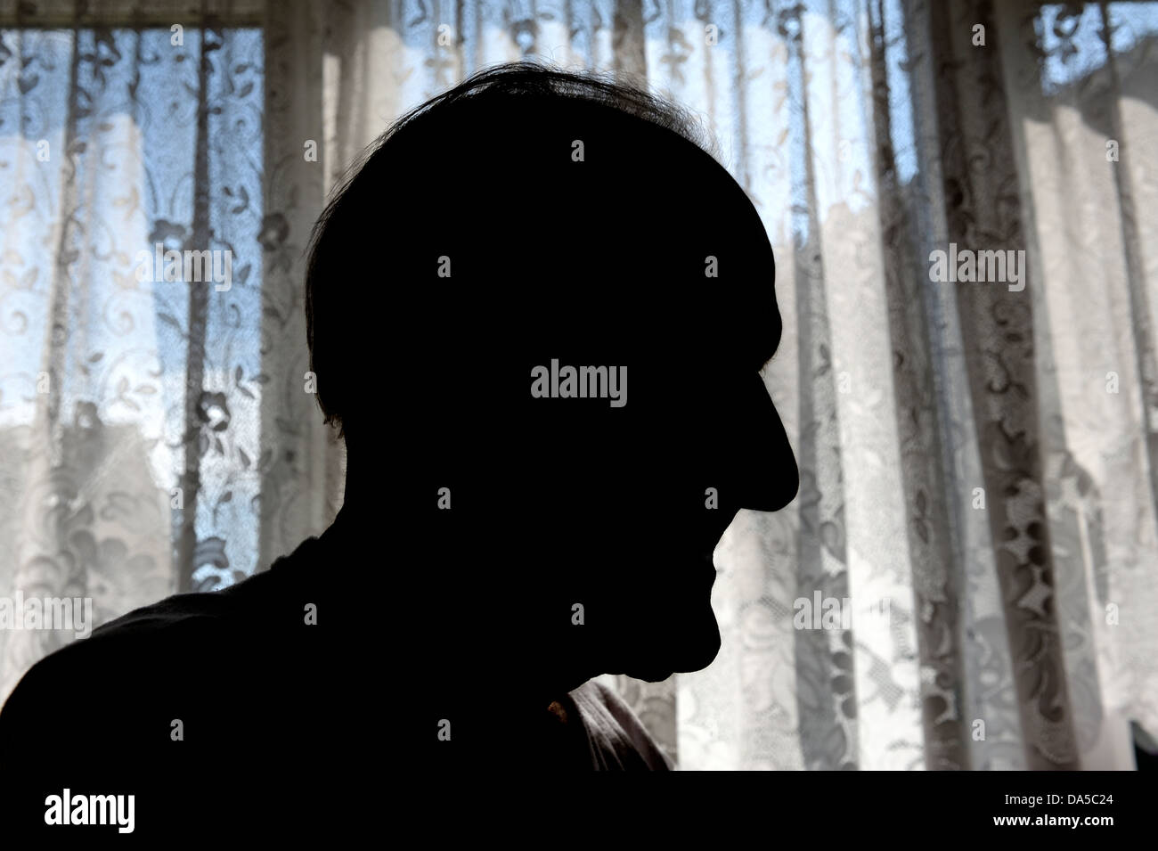 silhouette of an old man standing in front of net curtains Stock Photo