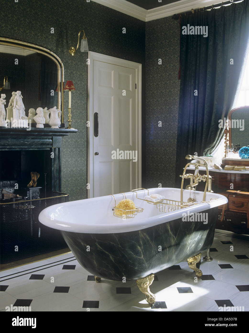 Roll-top bathtub with shower tap fitting in center of green bathroom with black+white tiled floor Stock Photo