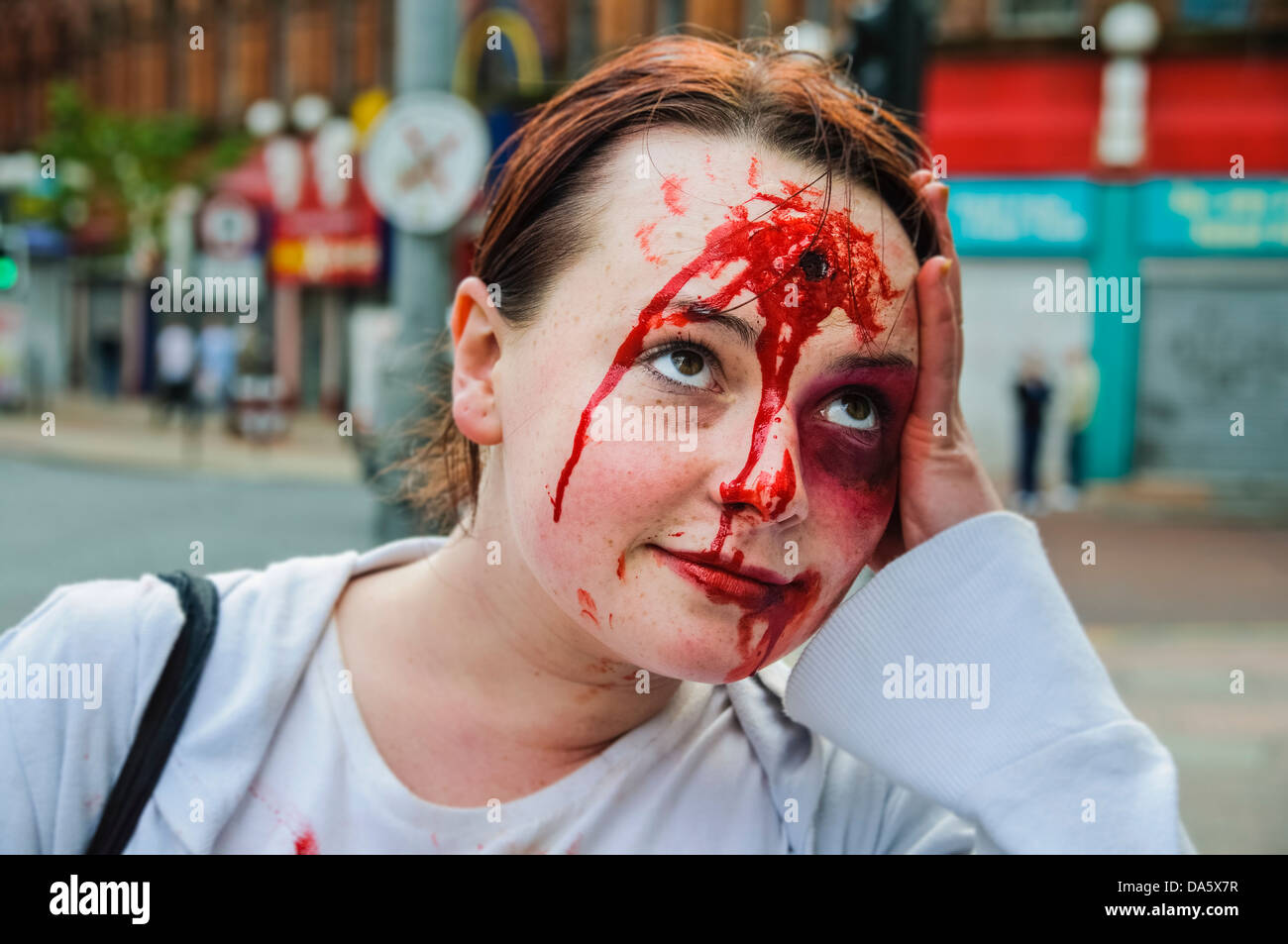 An actress with a simulated gunshot wound to her head and bruising holds her hand to her head as if she is having a very bad day Stock Photo