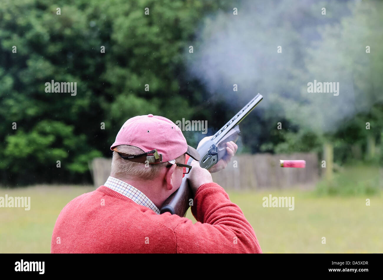 A spent shell is ejected from the gun as a man fires a shotgun while shooting clay pigeons Stock Photo