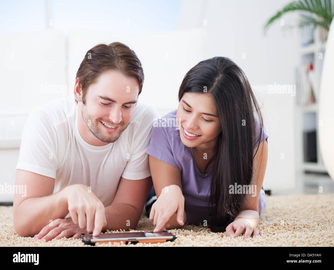 Lovely couple lying on carpet in living room and watching their favorite show on tablet pc. Stock Photo