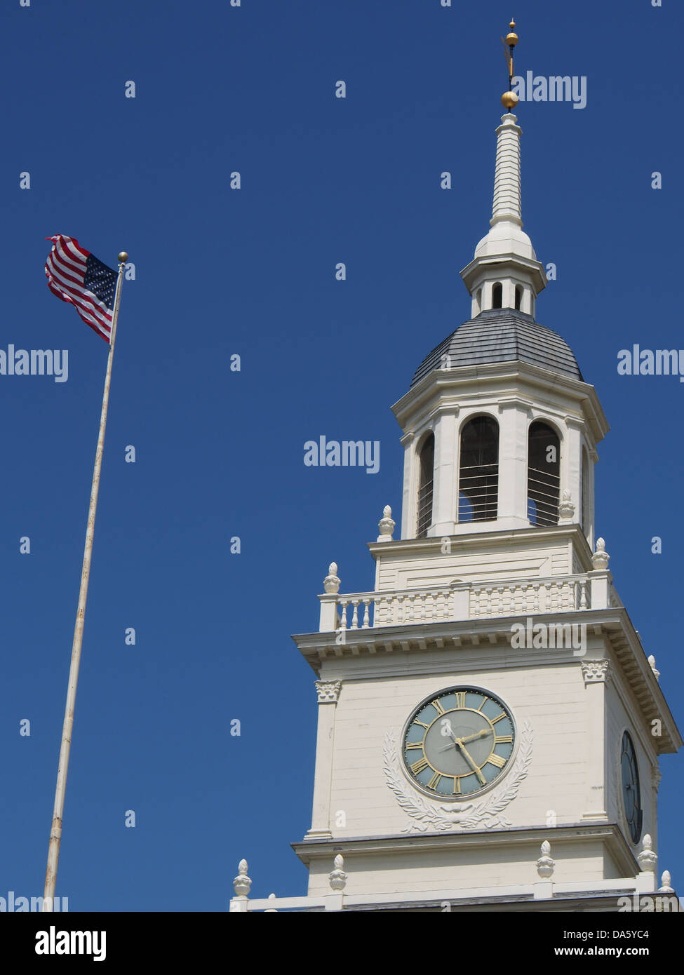 American flag blows in the wind in front of a town square clock tower Stock Photo