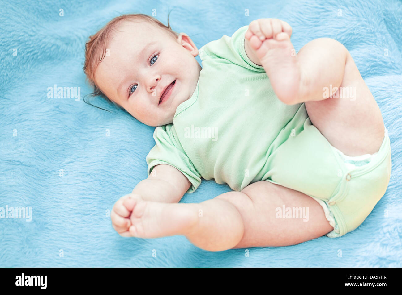 Cute smiling baby lying on a blue blanket after having a bath. Stock Photo