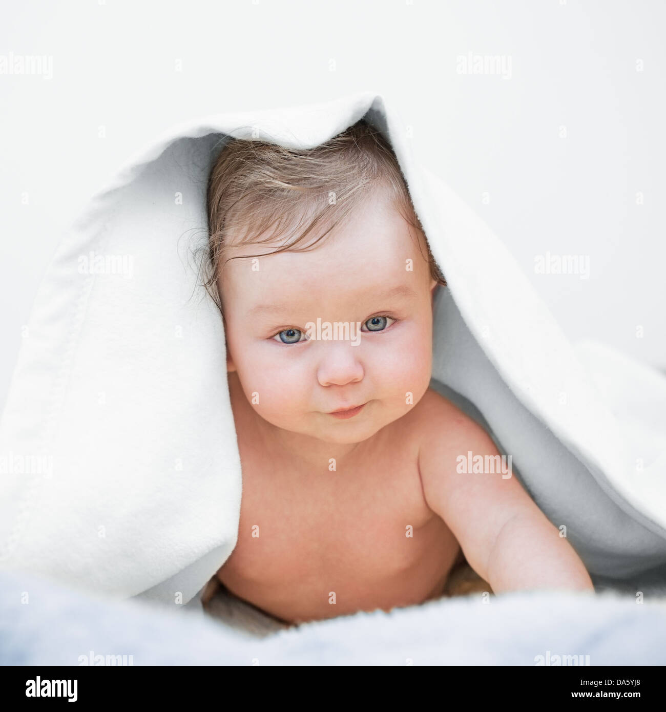 Close-up of adorable baby covered with a white blanket, lying down on bed after bath. Stock Photo