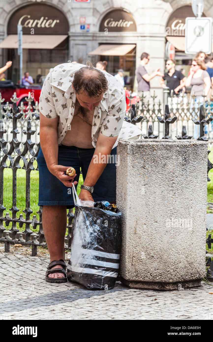 A homeless man looks through litter for food in Town Square, Prague. Cartier shop in background. Contrast of wealth and poverty. Stock Photo