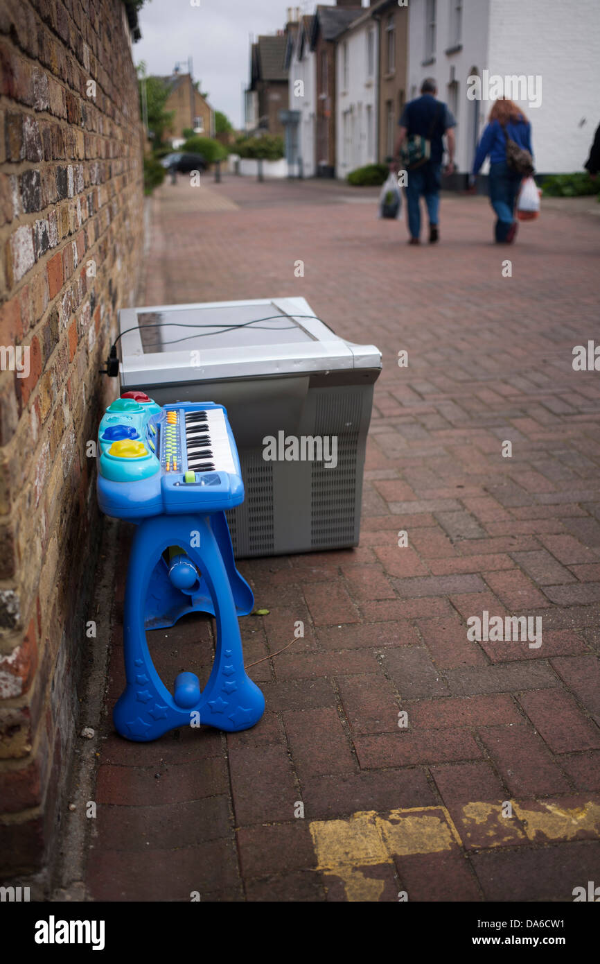 shoppers walk past child's toy piano and TV left  out on red brick paved street in Whitstable, Kent, England, UK Stock Photo