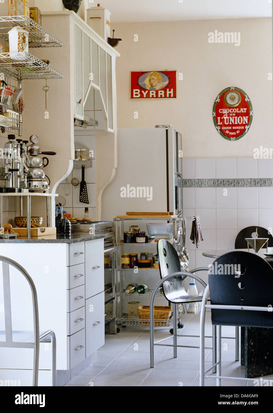 Metal table and chairs in centre of contemporary kitchen with freestanding storage unit and fifties advertisements on the wall Stock Photo