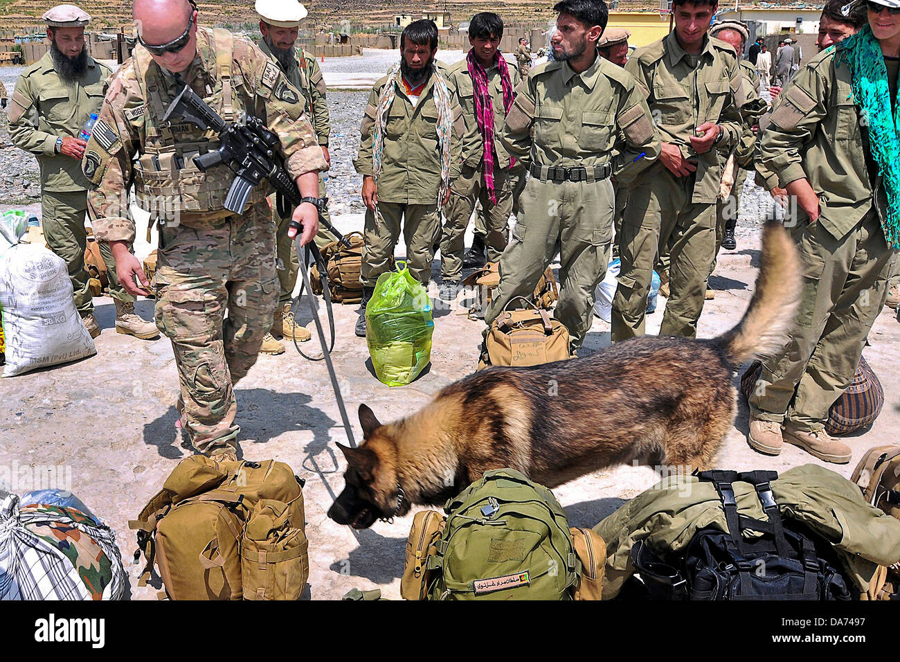 A US Army dog handler with Cougar Company of the 101st Airborne checks the bags of Afghan Air Force recruits before boarding aircraft June 2, 2013 in FOB Bastik, Kunar Province, Afghanistan. Stock Photo