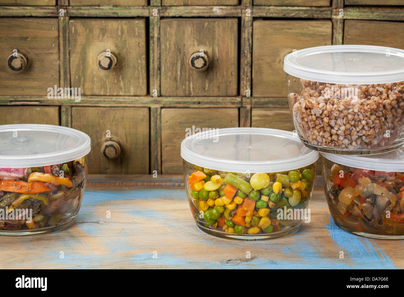 dinner leftovers (buckwheat kasha, vegetables, stir fry) in glass containers with drawer cabinet in background Stock Photo