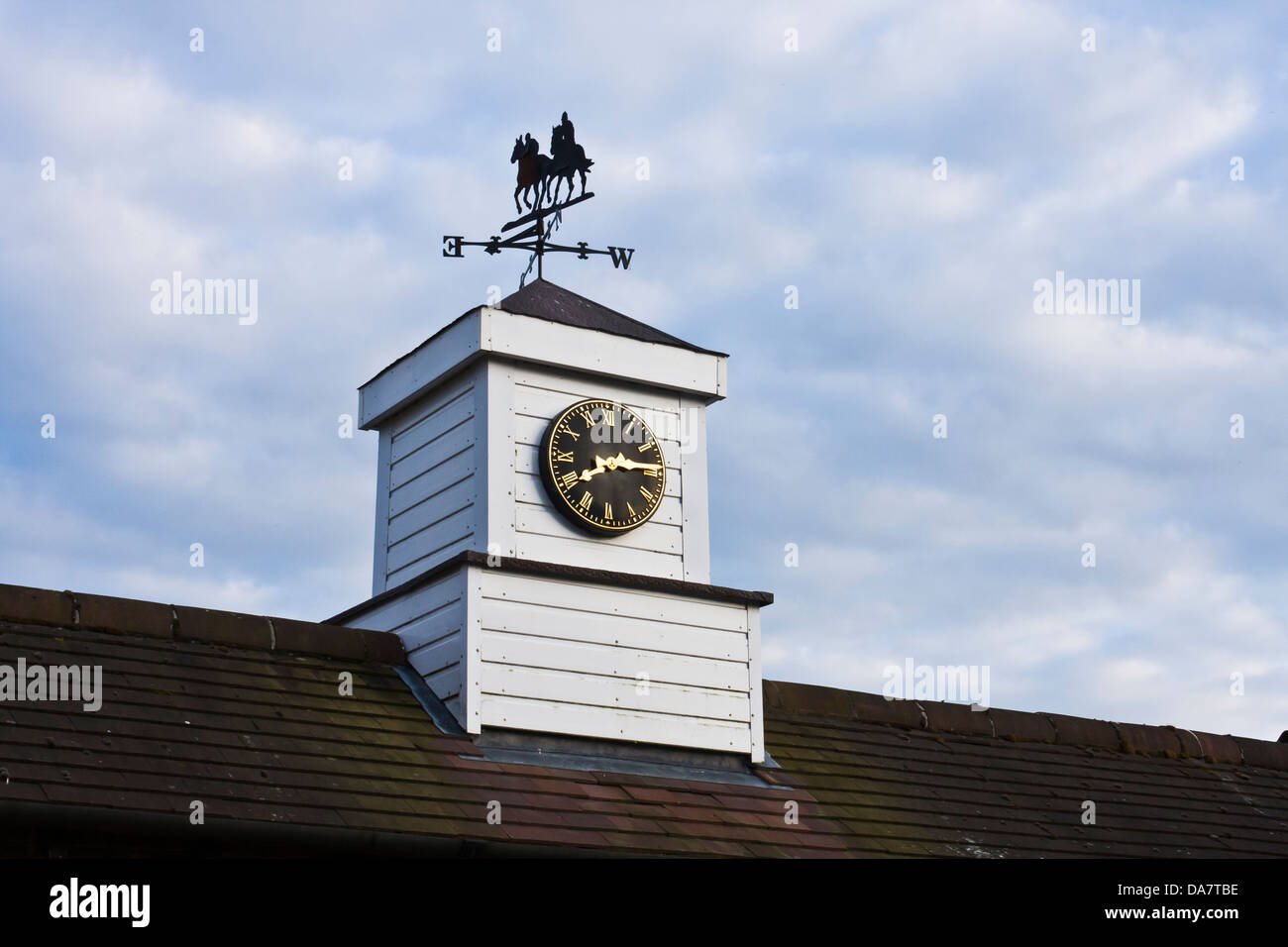 A weather vane with a racehorse motif sits atop a clock tower on the roof of a building in a stud. Stock Photo