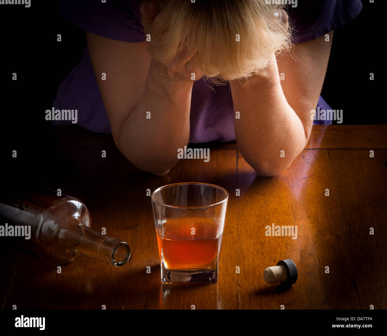 Concept photo for alcoholism disease showing whiskey glass and empty bottle with woman hands over face depressed over the glass Stock Photo