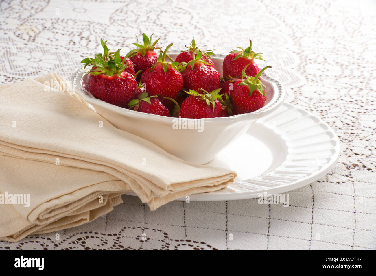 Bowl of fresh strawberries in white bowl with napkins on white lace tablecloth Stock Photo