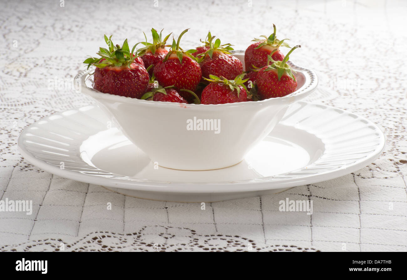 Bowl of fresh strawberries in white bowl white lace tablecloth Stock Photo