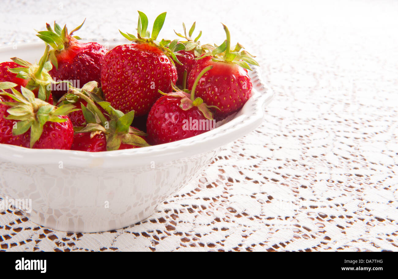Closeup of bowl of fresh strawberries in white bowl white lace tablecloth with copy space on right Stock Photo