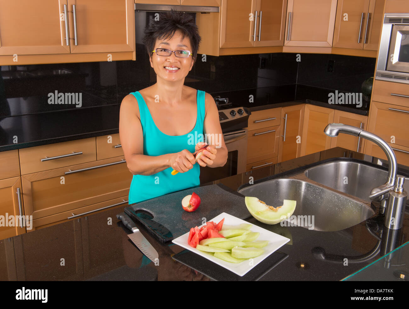 Asian woman in her kitchen chops fruit for fruit plate Stock Photo