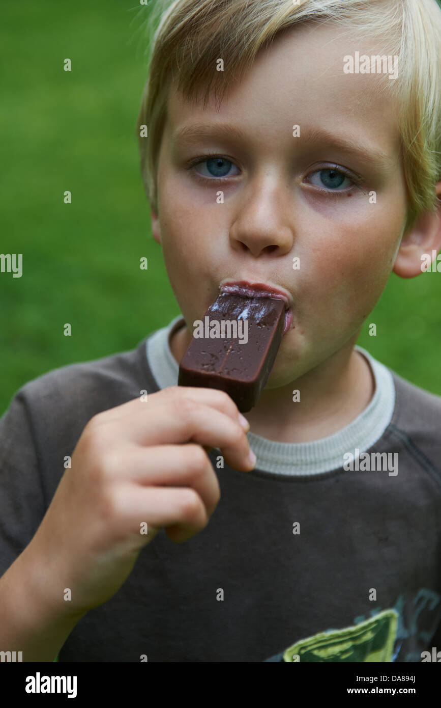 Blond child 68 year old boy holds and eating ice cream summertime