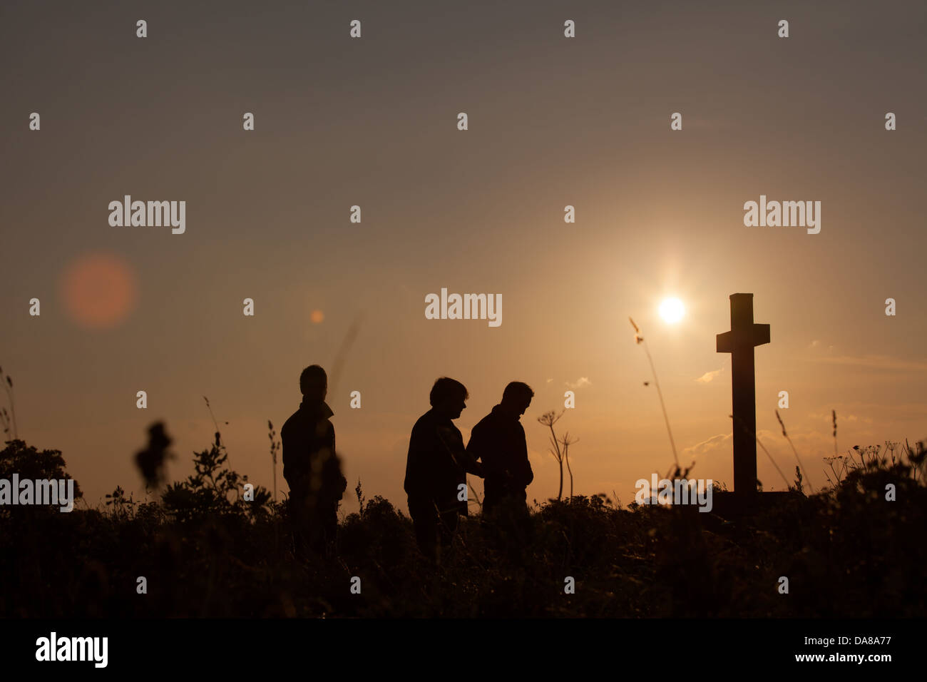 three figures in silhouette approach a cross at dawn Stock Photo - Alamy
