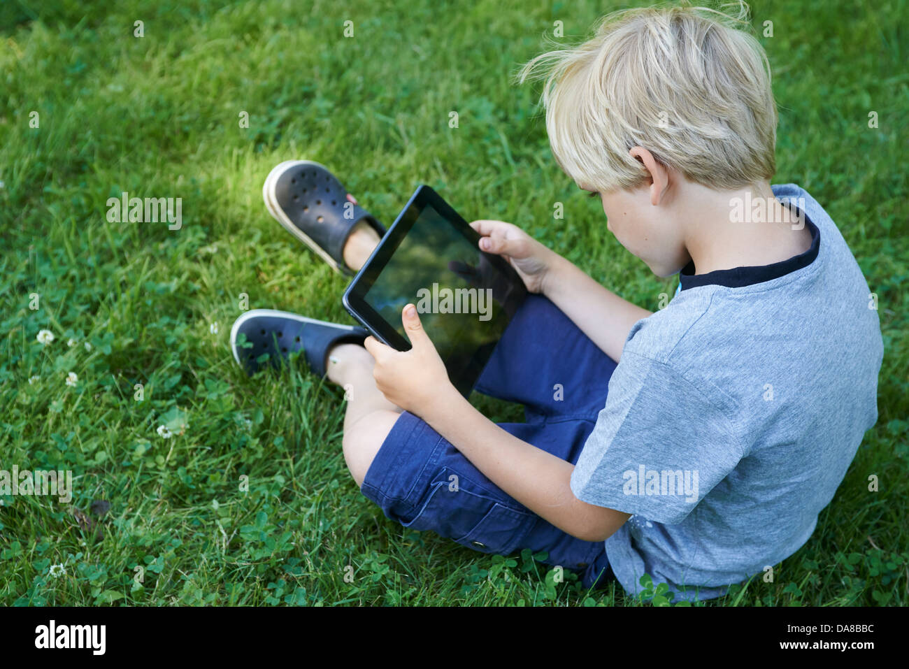 Cute child blond young boy playing with a digital tablet outdoors in ...