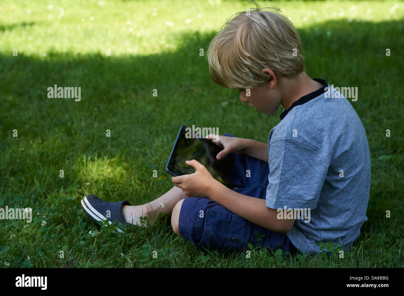 Cute child blond young boy playing with a digital tablet outdoors in ...