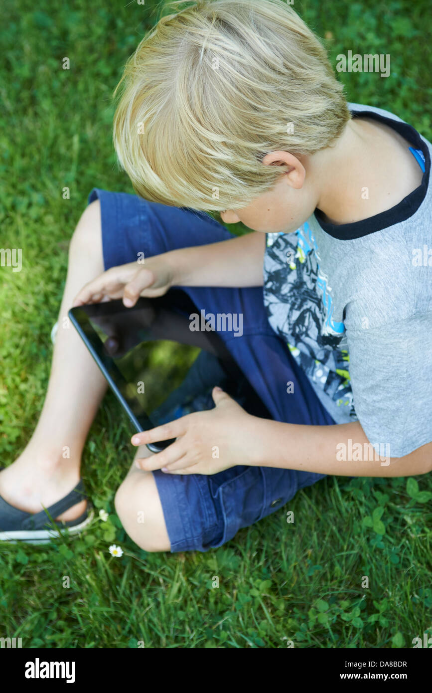 Cute child blond young boy playing with a digital tablet outdoors in ...