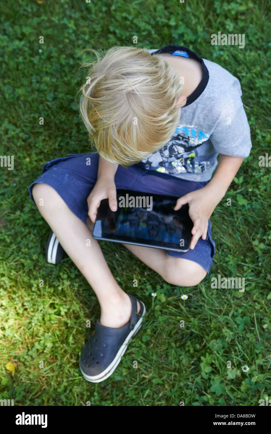 Cute child blond young boy playing with a digital tablet outdoors in ...