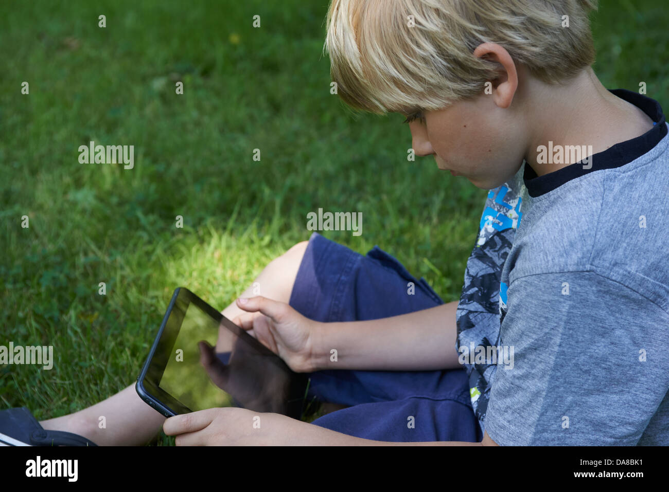 Cute child blond young boy playing with a digital tablet outdoors in ...