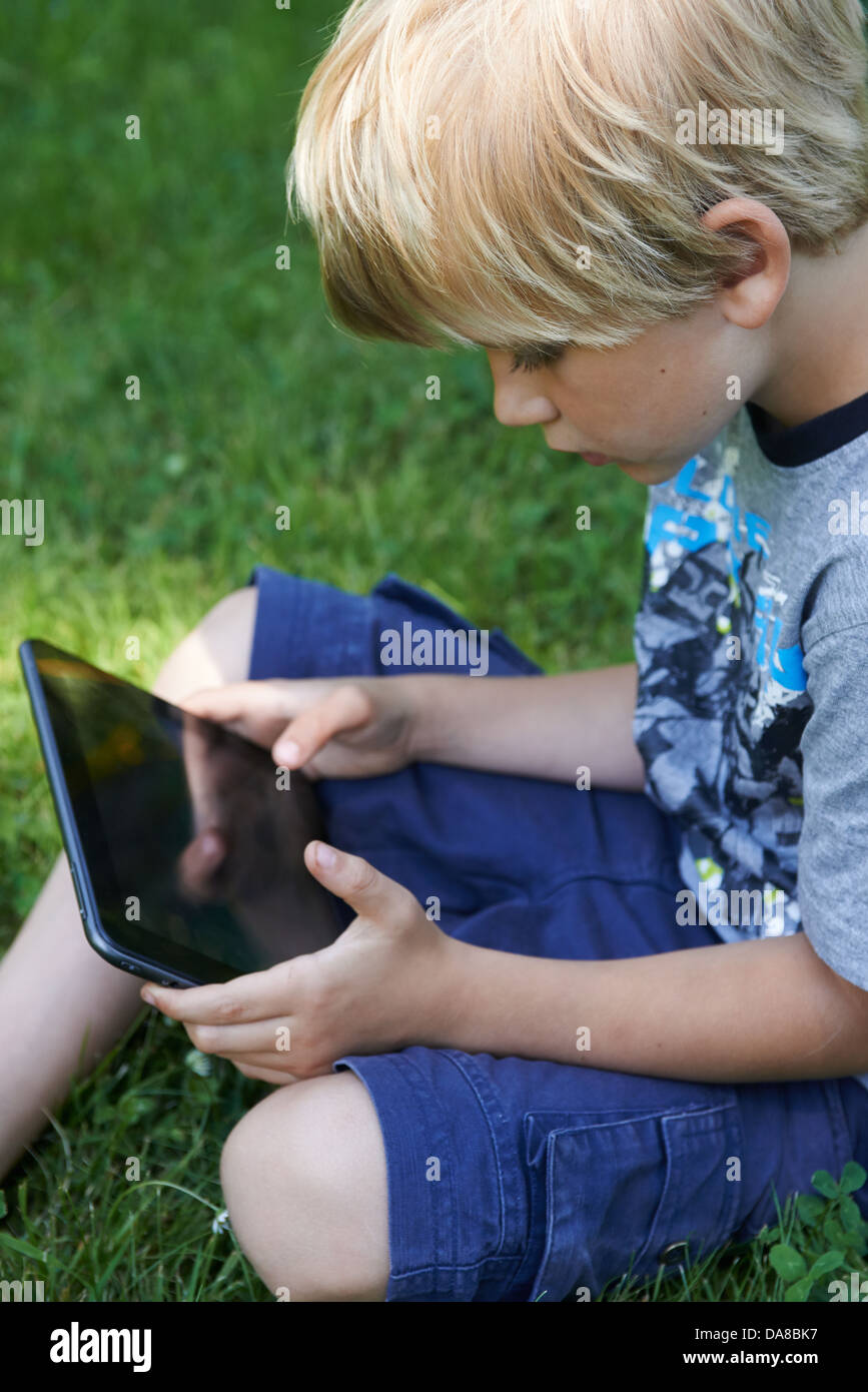 Cute child blond young boy playing with a digital tablet outdoors in ...