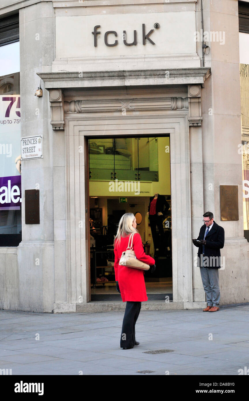 A woman wearing a red coat walks past French Connection shop. Regent Street, London. Stock Photo
